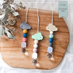 May include: Three colourful cloud-shaped silicone baby teethers with rainbow beads and crystal pendants. The teethers are hanging from white strings. The text "STL-Datei: Sonnenfänger Wolke" is visible in the top right corner of the image.