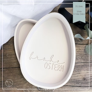 Pode incluir: Duas travessas ovais brancas. A palavra "Frohe OSTERN" está gravada na superfície da travessa. As travessas estão sobre uma superfície de madeira. As travessas são provavelmente para a Páscoa.