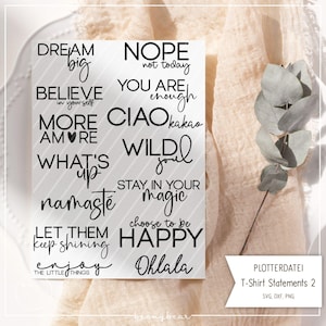 Puede incluir: Una tarjeta blanca con texto negro que presenta citas inspiradoras como "Dream Big", "Believe in Yourself" y "Happy". La tarjeta está colocada sobre un fondo de tela de tonos neutros, con una ramita de vegetación a la derecha. La tarjeta está etiquetada como "T-Shirt Statements 2".