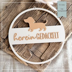 Könnte beinhalten: Weißer, kreisförmiger Wandschmuck mit einer braunen Dackel-Silhouette und dem Schriftzug "herein GEDACKELT" in brauner Schrift. Das Schild ist vor einem rustikalen Holzgrund platziert. Ein kleines Etikett oben rechts lautet "STL-Datei: Loop hereingedackelt".