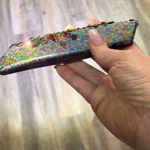 May include: A iridescent, multi-colored, decorative knife with rhinestones. The knife has a black handle and a silver blade.