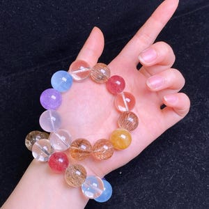 Puede incluir: Una pulsera de cuentas con una variedad de cuentas de piedras preciosas translúcidas y coloridas. Las cuentas son redondas y varían en color, desde transparente hasta morado, rojo, amarillo y azul. La pulsera se muestra en una muñeca.