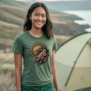 May include: A green t-shirt featuring a graphic of a stylised eagle with geometric patterns in shades of brown, orange, and black. The eagle is surrounded by a circle of smaller geometric shapes.