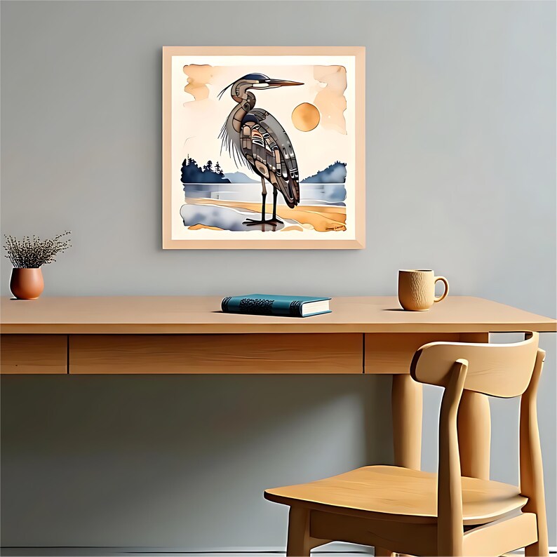 K&ouml;nnte beinhalten: Aquarelldruck eines Graureihers, der an einem sandigen Ufer steht, mit Sonne und Landschaft im Hintergrund. Das Kunstwerk ist in einem hellen Holzrahmen gerahmt und h&auml;ngt an einer grauen Wand. Ein Schreibtisch mit Buch, Tasse und Pflanze befindet sich im Vordergrund.