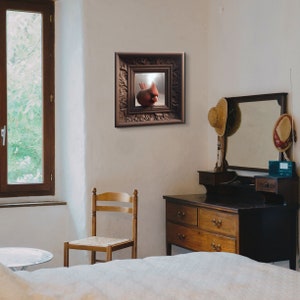 May include: A framed print of a red cardinal bird perched on a branch. The frame is ornate and has a dark brown finish. The print is hanging on a white wall in a room with a dresser and a chair.