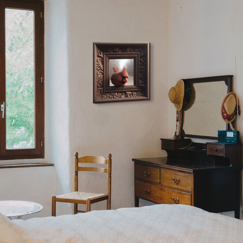 May include: A framed print of a red cardinal bird perched on a branch. The frame is ornate and has a dark brown finish. The print is hanging on a white wall in a room with a dresser and a chair.