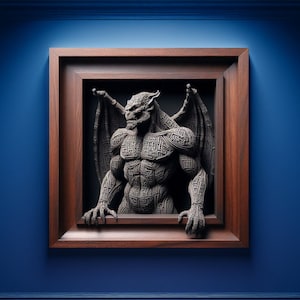 May include: A framed, three-dimensional sculpture of a gargoyle with intricate patterns. The sculpture is dark gray and set within a dark wood frame against a blue wall. The gargoyle has large wings and is emerging from the frame.
