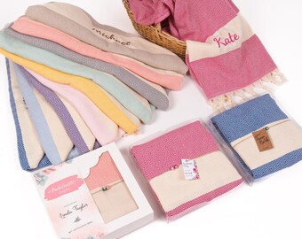 May include: A stack of colorful Turkish towels with fringe, some folded and some in gift boxes. The towels are personalized with names like "Michael" and "Kate".