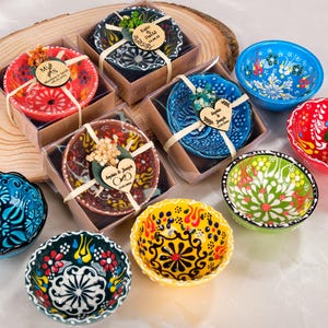 Puede incluir: Colección de cuencos de cerámica pintados a mano con intrincados diseños florales. Algunos cuencos están empaquetados en cajas pequeñas con detalles decorativos y etiquetas de madera. Los cuencos son de varios colores, incluyendo rojo, azul, verde y amarillo.