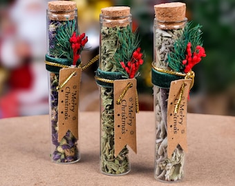 May include: Three glass vials filled with dried herbs and flowers, each topped with a cork and decorated with a green ribbon, sprigs, and red berries. Each vial has a tag that says "Merry Christmas".