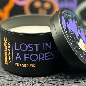 May include: A black candle jar with a white lid. The candle jar has a black label with white text that reads 'DARKWAVE CANDLE CO. LOST IN A FOREST FRASER FIR'.