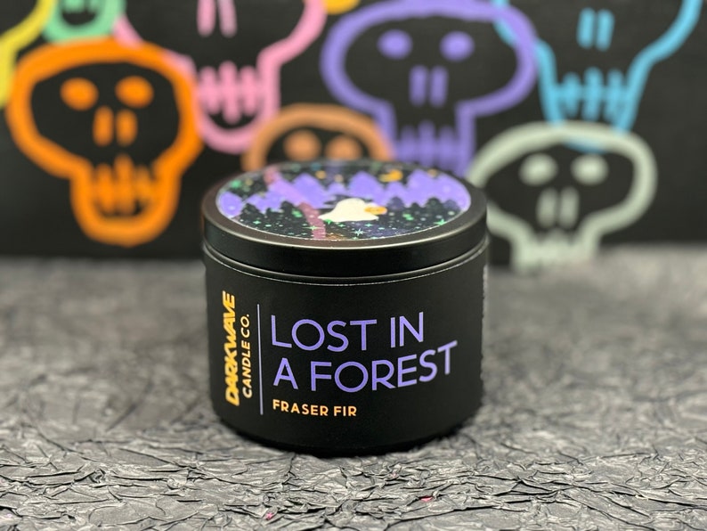 May include: A black candle jar with a white and purple design on the lid. The jar is labelled "Darkwave Candle Co. Lost in a Forest Fraser Fir".
