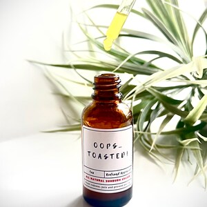 May include: A brown glass bottle with a white label that reads "Oops... Toasted!"  Redhand Approved. All Natural Sunburn Eraser. Ease redness, pain and prevent future sun damage.  The bottle has a dropper with a yellow liquid.
