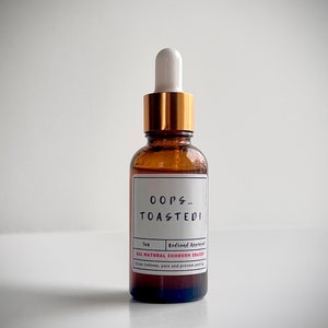 May include: A brown glass bottle with a gold cap and a white dropper. The label reads "OOPS... TOASTED!" and "ALL NATURAL SUNBURN ERASER".