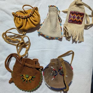 Puede incluir: Un surtido de peque&ntilde;as bolsas y bolsos de cuero hechos a mano. Las bolsas son de varios colores, incluyendo amarillo, marr&oacute;n y beige, y est&aacute;n adornadas con abalorios coloridos. Algunas tienen cordones, otras asas o correas.