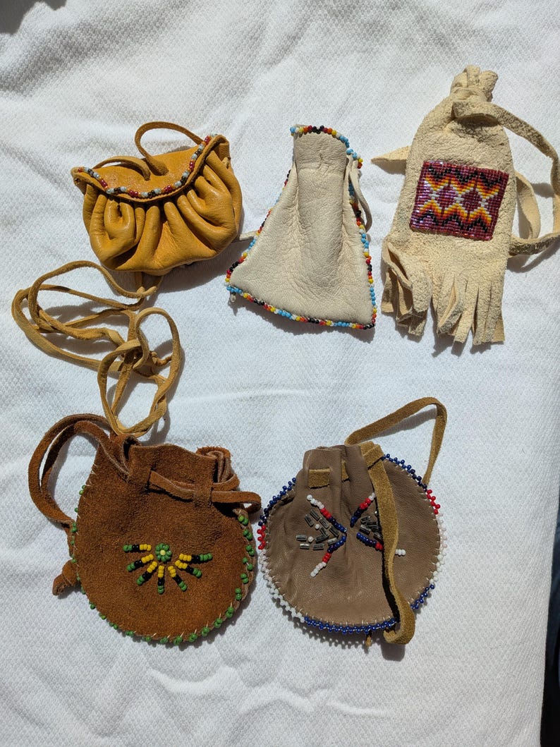 Puede incluir: Un surtido de peque&ntilde;as bolsas y bolsos de cuero hechos a mano. Las bolsas son de varios colores, incluyendo amarillo, marr&oacute;n y beige, y est&aacute;n adornadas con abalorios coloridos. Algunas tienen cordones, otras asas o correas.