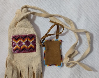 Puede incluir: Una bolsa de cuero color crema con una correa larga y flecos, que presenta un panel rectangular de cuentas con un patrón geométrico en rojo, amarillo y negro, junto a una bolsa de cuero marrón más pequeña con un borde de cuentas multicolor.