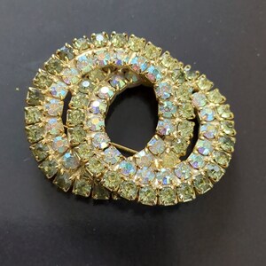 May include: A gold tone brooch with two overlapping circles of iridescent green rhinestones.