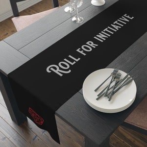 May include: Black table runner with the text "Roll for Initiative" in white and a red 20-sided die graphic on each end.