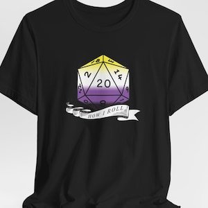 May include: Black t-shirt featuring a graphic of a twenty-sided die in the non-binary pride flag colors: yellow, white, purple, and black. The die has the number 20 on it, with the text "HOW I ROLL" on a banner below.