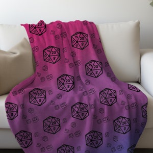May include: A pink and blue gradient throw blanket with a repeating pattern of black 20-sided dice.