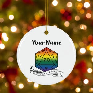 May include: White round ornament with a gold string. The ornament features the text "Your Name" above a colorful, rainbow-colored D20 die. Below the die is a banner that reads "HOW I ROLL".