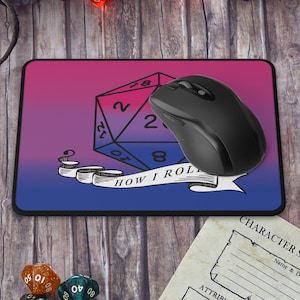 Può includere: Un tappetino per mouse con sfumatura rosa e blu con un'illustrazione in bianco e nero di un dado a 20 facce e il testo "How I Roll". Un mouse per computer nero è sul tappetino per mouse.