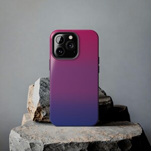 May include: A smartphone case featuring a smooth colour gradient that transitions from a vibrant magenta at the top to a deep royal blue at the bottom. The case includes a black camera module cutout with three circular lenses and a flash.