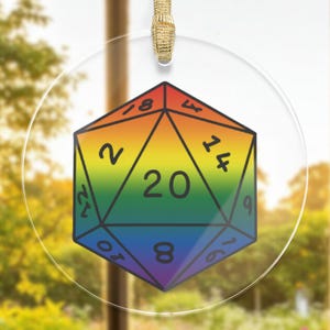Peut inclure: Une décoration ronde transparente présente un dé à 20 faces, également appelé d20, aux couleurs de l'arc-en-ciel. Le dé comporte les chiffres 2, 4, 6, 8, 10, 12, 14, 16, 18 et 20 sur ses faces.