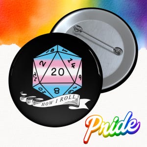 May include: A black button with a silver pin back. The button features a blue, pink, and white transgender pride flag design in the shape of a 20-sided die. The text "HOW I ROLL" is on a banner below the die.