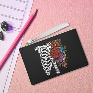 May include: Black leather zippered pouch with a white skeleton ribcage design and a colourful 20-sided die with flowers.