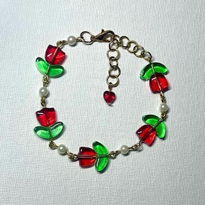 May include: A gold chain bracelet with red and green glass flower charms and white pearl beads.