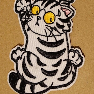 May include: White and black embroidered iron-on patch of a cartoon cat with yellow eyes, black stripes, and pink ears. The cat is sitting up with its paws raised in the air.