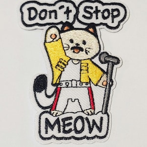 May include: Embroidered patch depicting a cartoon cat in a yellow jacket, white top, and red trousers, holding a microphone. The patch has the text "Don't Stop" above and "MEOW" below, all in black lettering.