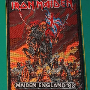 May include: A rectangular embroidered patch featuring the Iron Maiden logo at the top and a skeletal figure on horseback holding a Union Jack flag. The scene includes a fiery orange and red background with the text MAIDEN ENGLAND '88 at the bottom.