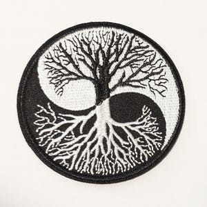 May include: Embroidered patch with a Yin and Yang design, featuring a tree motif in black and white. The tree's branches and roots are intricately detailed, creating a balanced and symbolic representation. The patch has a black border.