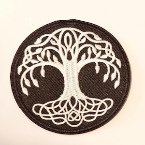 May include: Round black patch with a white embroidered tree of life design. The tree features intricate roots, a detailed trunk, and leafy branches. The patch is suitable for jackets, bags, or other fabric items.