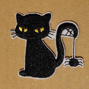 May include: Black embroidered iron-on patch of a black cat with yellow eyes and a spider web on its tail. The cat is sitting with its tail curled around a spider web.