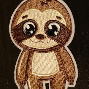 Puede incluir: Un parche bordado de un perezoso marrón y beige con ojos grandes y una cara sonriente. El perezoso está de pie sobre sus dos pies y tiene un contorno blanco.
