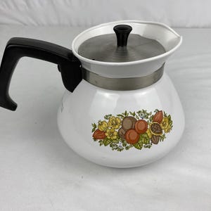 May include: White enamel coffee pot with a black handle and lid. The pot features a floral design with brown, orange, and yellow fruits and flowers. The lid is stainless steel.