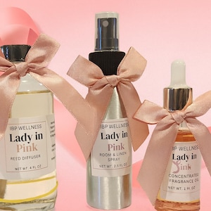 May include: Three bottles of IBP Wellness products, each adorned with a pink ribbon bow. The products include a reed diffuser, room and linen spray, and concentrated fragrance oil. The labels read "Lady in Pink".