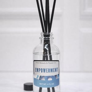 May include: A clear glass aromatherapy diffuser bottle with black reeds. The label reads "EMPOWERMENT" and "NET WT. 4 FL OZ". The bottle has a black cap next to it. The product is from Inner Beauty & Peace Co.