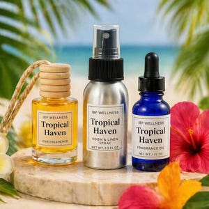 Pode incluir: Três frascos de produtos IBP Wellness Tropical Haven: um ambientador para carro, um spray para quarto e roupa de cama e um óleo de fragrância. O ambientador para carro está num frasco de vidro pequeno com tampa de madeira.