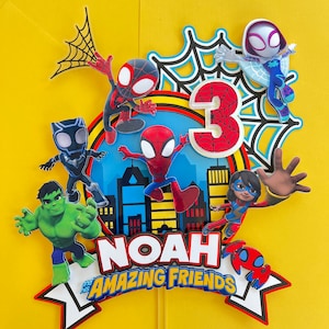 Puede incluir: Un adorno para pastel colorido con personajes de Spider-Man, incluyendo Spider-Man, Spider-Gwen y Miles Morales. El adorno tambi&eacute;n incluye un n&uacute;mero 3, el nombre "Noah" y el texto "y sus incre&iacute;bles amigos".
