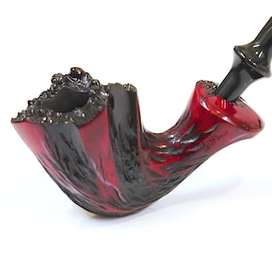May include: A handcrafted tobacco pipe with a red and black finish. The bowl has a textured, carved design, and the stem is black and curved. The pipe is designed for smoking tobacco and has a classic shape.