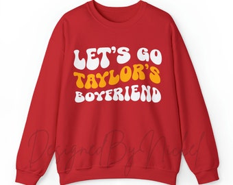 May include: Red sweatshirt with the text "Let's go Taylor's Boyfriend" in white and yellow letters.