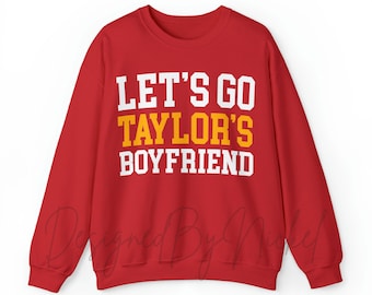 May include: Red sweatshirt with white text that says "Let's Go Taylor's Boyfriend". The word "Taylor's" is in yellow.