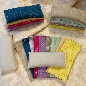 May include: A collection of handmade eye pillows in various colors and patterns. The pillows are made of fabric and filled with rice and lavender. They are designed to be used for relaxation and stress relief.