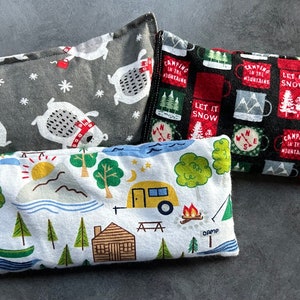 May include: Three fabric-covered heat packs with different designs. One is gray with white polar bears, one is white with a camping scene, and one is black with red mugs and the text "Let it snow" and "Camping in the mountains".
