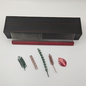 May include: A wooden box with a metal ruler and a set of metal quills. The box is closed and the ruler is extended. There are four paper quilled flowers on a white surface.
